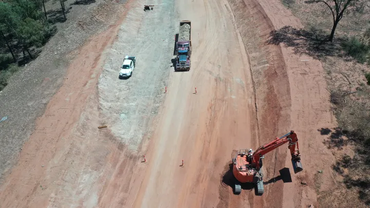 Grader smoothing gravel surface on Clermont Alpha Road construction, with open countryside in the background