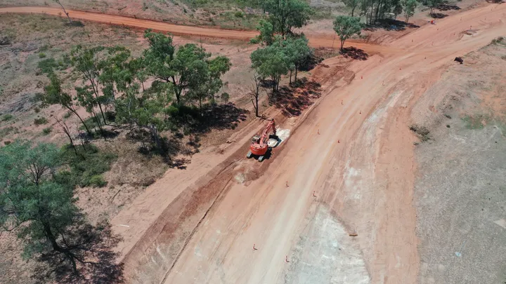 Compactor rolling fresh asphalt on Clermont Alpha Road, surrounded by rural landscape during paving works