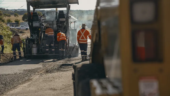 Road construction workers in high-visibility gear paving asphalt with heavy machinery