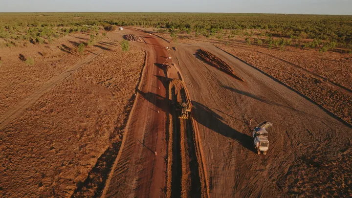 Aerial view of a road construction project with graders and trucks working on earthworks in a rural area.
