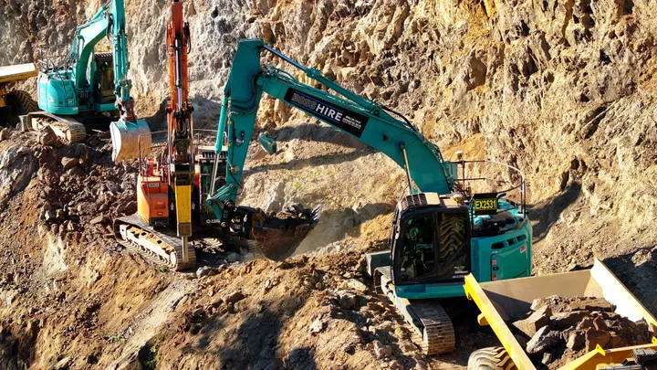 Excavators loading rocks into an articulated hauler at a construction site, working on earthmoving and excavation tasks.