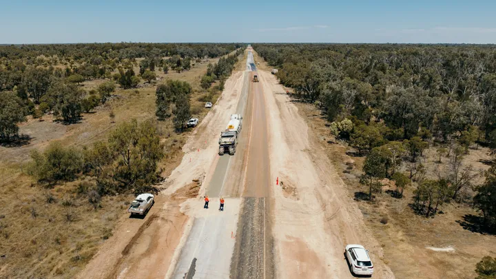 A regional road construction project in progress under clear blue skies, showcasing civil engineering and infrastructure renewal efforts in a rural setting.