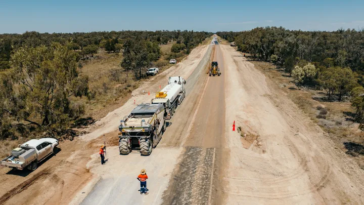 Construction workers manage a regional road renewal project, with heavy machinery and vehicles actively working to improve roads under clear blue skies.