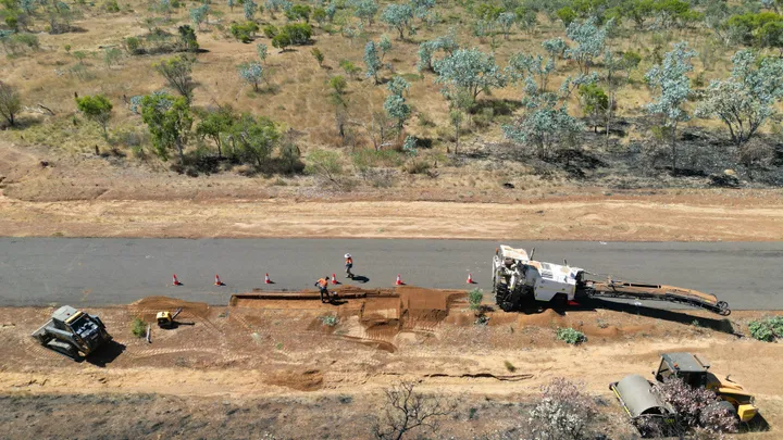 Road construction workers in high-visibility gear excavating a trench