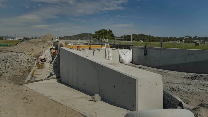 Construction workers building concrete retaining walls for a new culvert crossing at Gold Coast Airport.