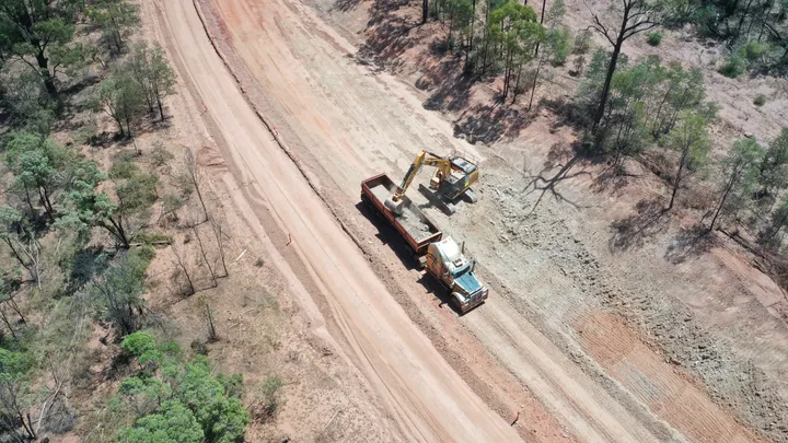 Excavator leveling earth on Clermont Alpha Road project, preparing for upgrades under clear skies