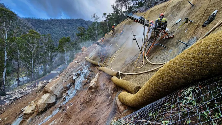 Workers stabilising a steep hillside using soil nails and erosion control matting to prevent landslides.
