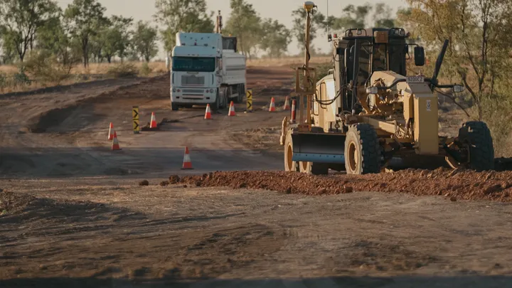 Grader and truck on a road construction site, surrounded by safety cones and marked paths for active earthworks