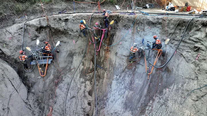 Construction workers using drilling rigs and harnesses to stabilise an excavation site with soil nails and anchors