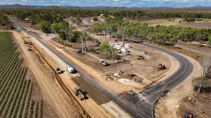 Aerial view of a construction site in a rural area, featuring road upgrades, heavy machinery, and nearby agricultural fields, illustrating infrastructure development and project management.