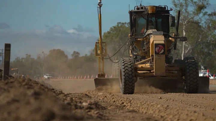 At a regional construction site, a grader works to level the road surface, demonstrating advanced engineering techniques for infrastructure improvement.