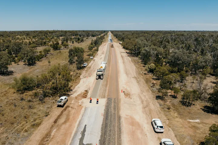 A regional road construction project in progress under clear blue skies, showcasing civil engineering and infrastructure renewal efforts in a rural setting.